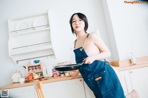 A naked woman sitting on top of a kitchen counter holding an apple.