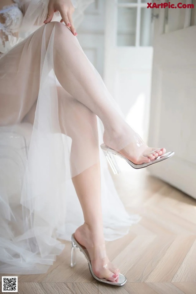 A woman in a wedding dress sitting on a chair with her legs crossed.