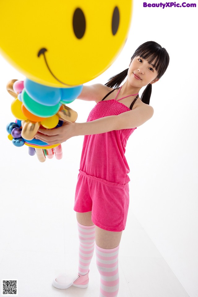 A woman in a pink dress holding a smiley face balloon.