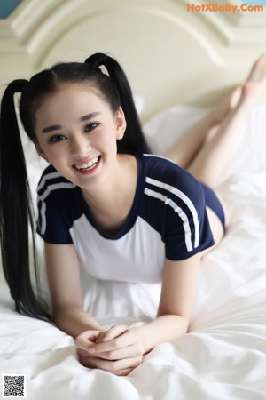 A woman in a white and blue shirt sitting on a bed.