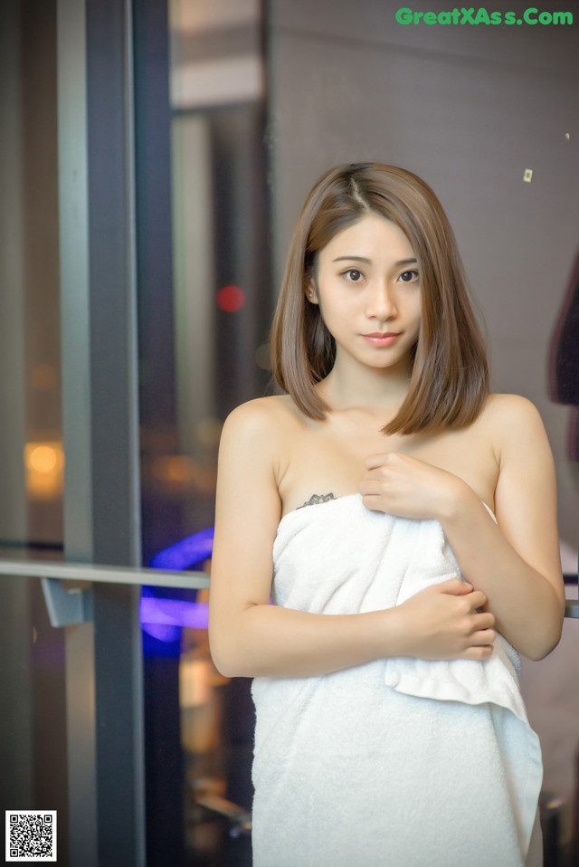 A woman in a white towel standing in front of a glass door.