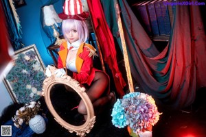 A woman in a red jacket and top hat sitting on a chair.