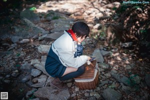 A woman in a red hooded outfit sitting on a rock.