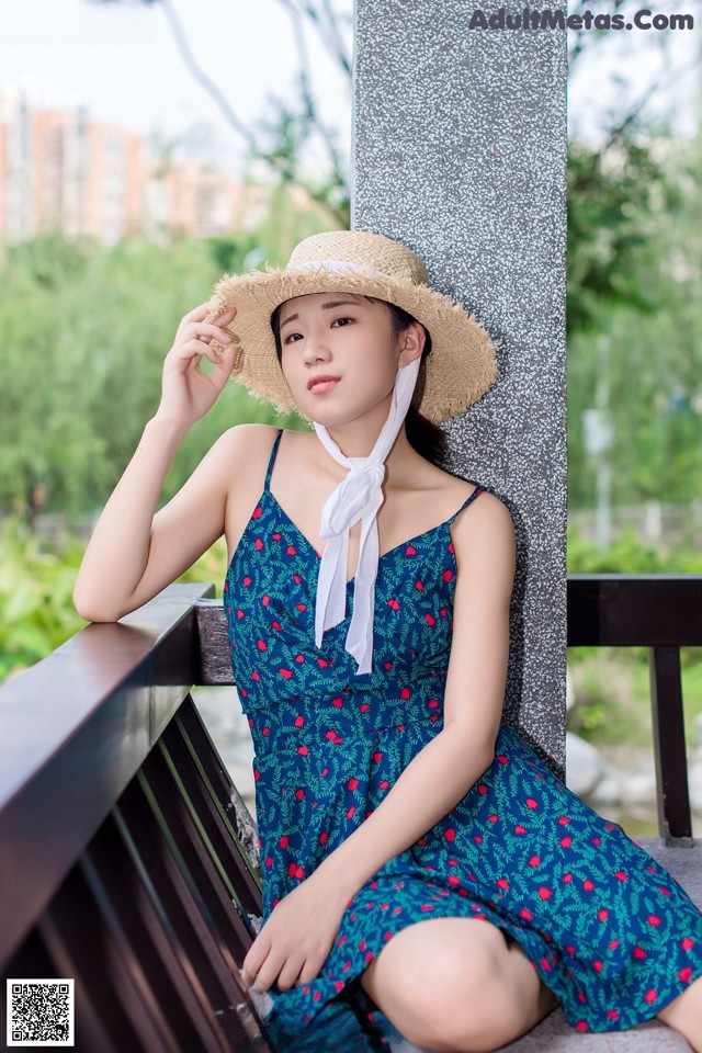 A woman in a blue dress and straw hat sitting on a bench.