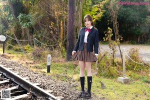 A woman in a school uniform leaning against a fence.