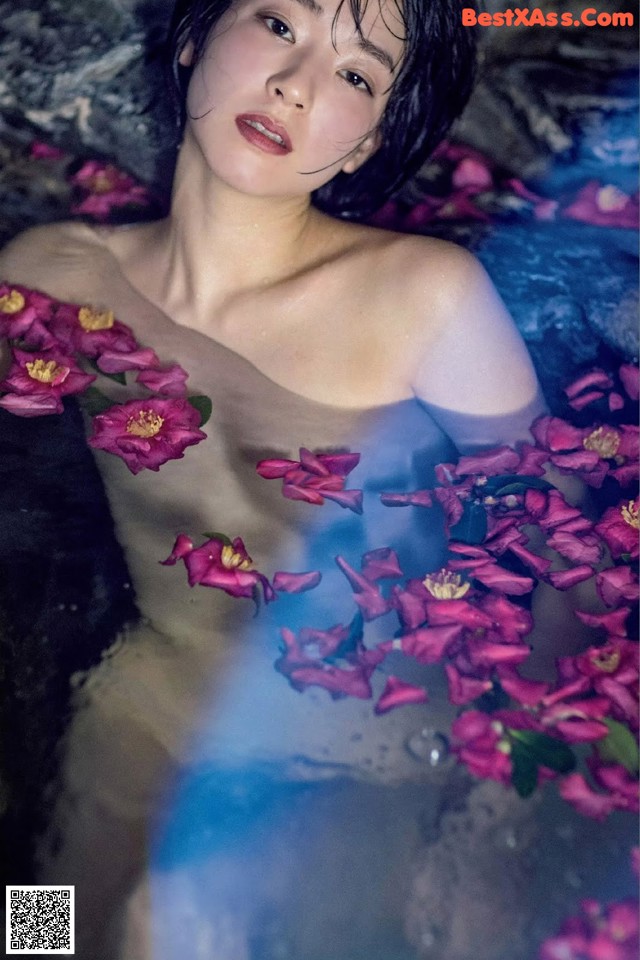 A woman in a bathtub with flowers floating around her.