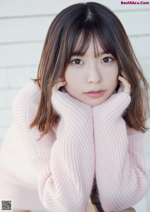 A woman in a pink sweater sitting on a window sill.