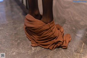 A woman in a brown dress and black stockings sitting on the floor.