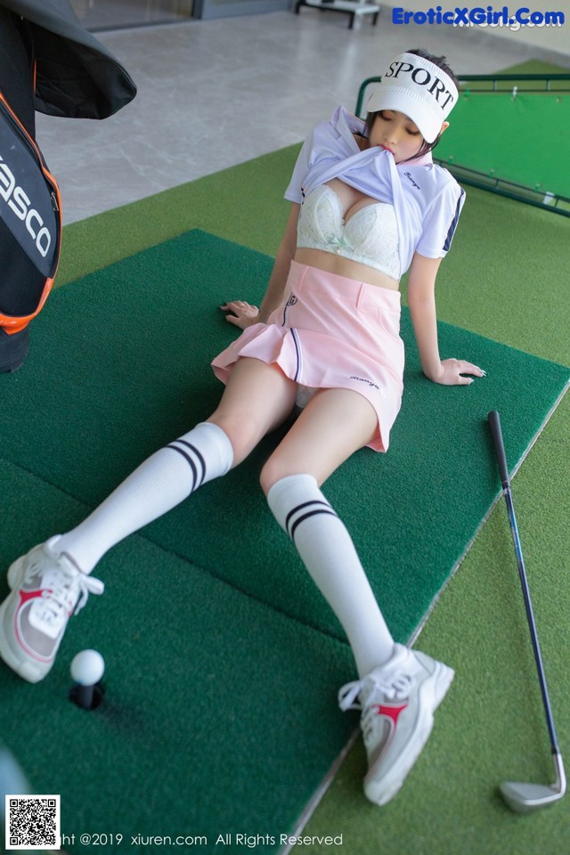 A woman in a pink skirt and white shirt is playing golf.