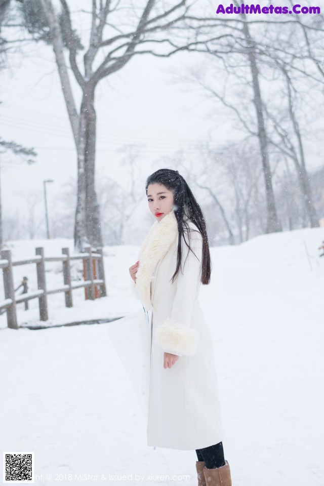 A woman in a white coat is standing in the snow.