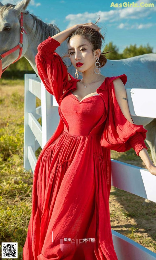 A woman in a red dress standing next to a white horse.