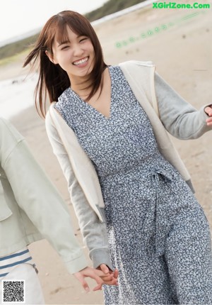 A woman standing on a beach holding a picture of herself.