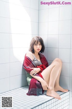 A woman sitting on the edge of a bathtub with her legs crossed.