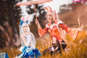 A couple of women sitting next to each other in a field.